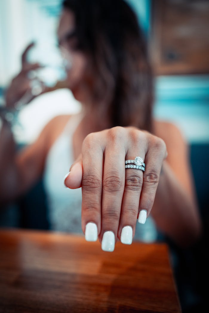 gallery-02 Close-up shot of a woman's hand displaying her engagement and wedding rings with manicured nails.